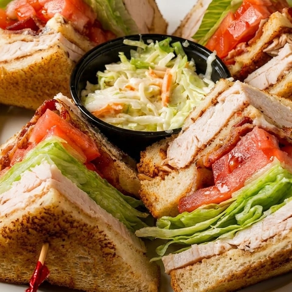 Four club sandwich halves with turkey, bacon, lettuce, tomato, a side of coleslaw, and a pickle.