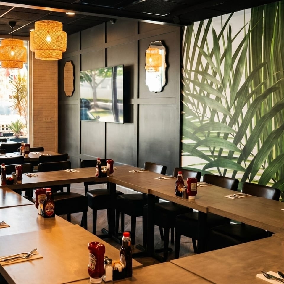 Restaurant interior with U-shaped tables set for dining, large windows, and a tropical leaf mural.